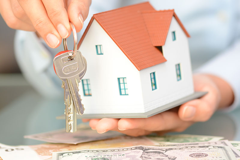 Das Bild zeigt zwei Hände. In der einen Hand ein Haustürschlüssel und in der anderen Hand ein kleines Haus
